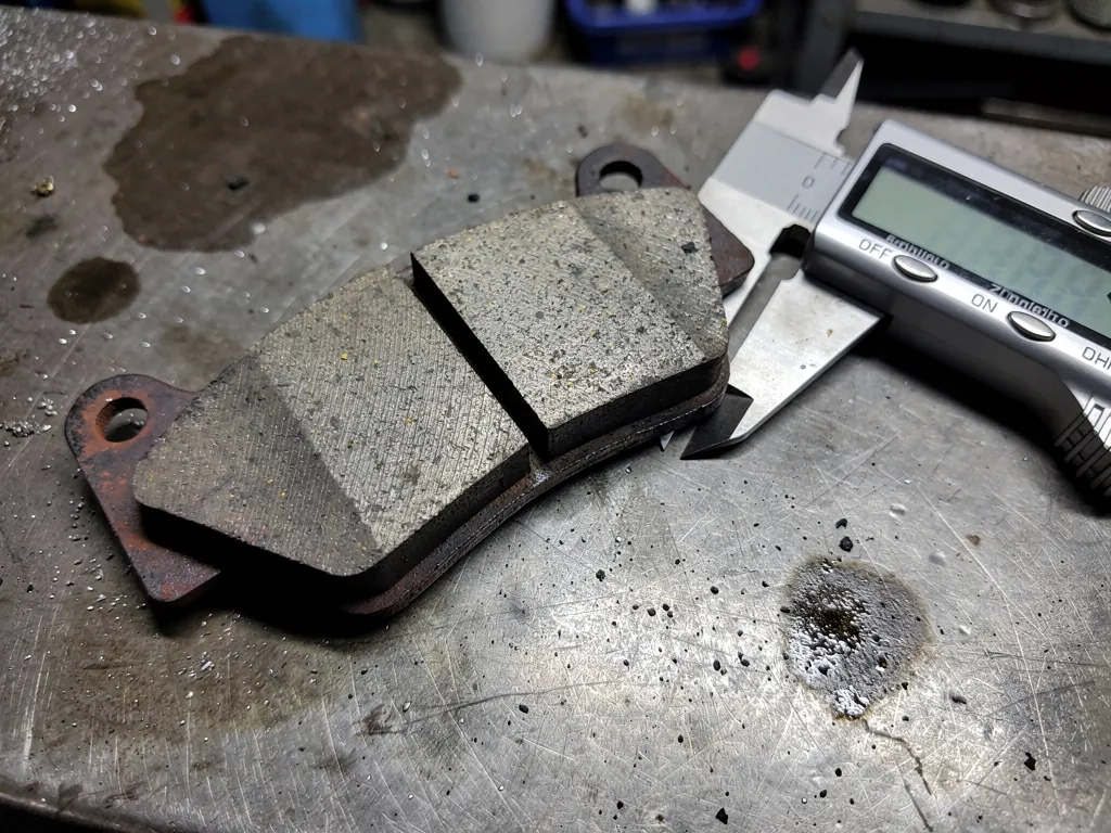 Worn brake pad from a brake pad warranty claim being measured with a caliper Worn brake pad from a brake pad warranty claim being measured with a caliper